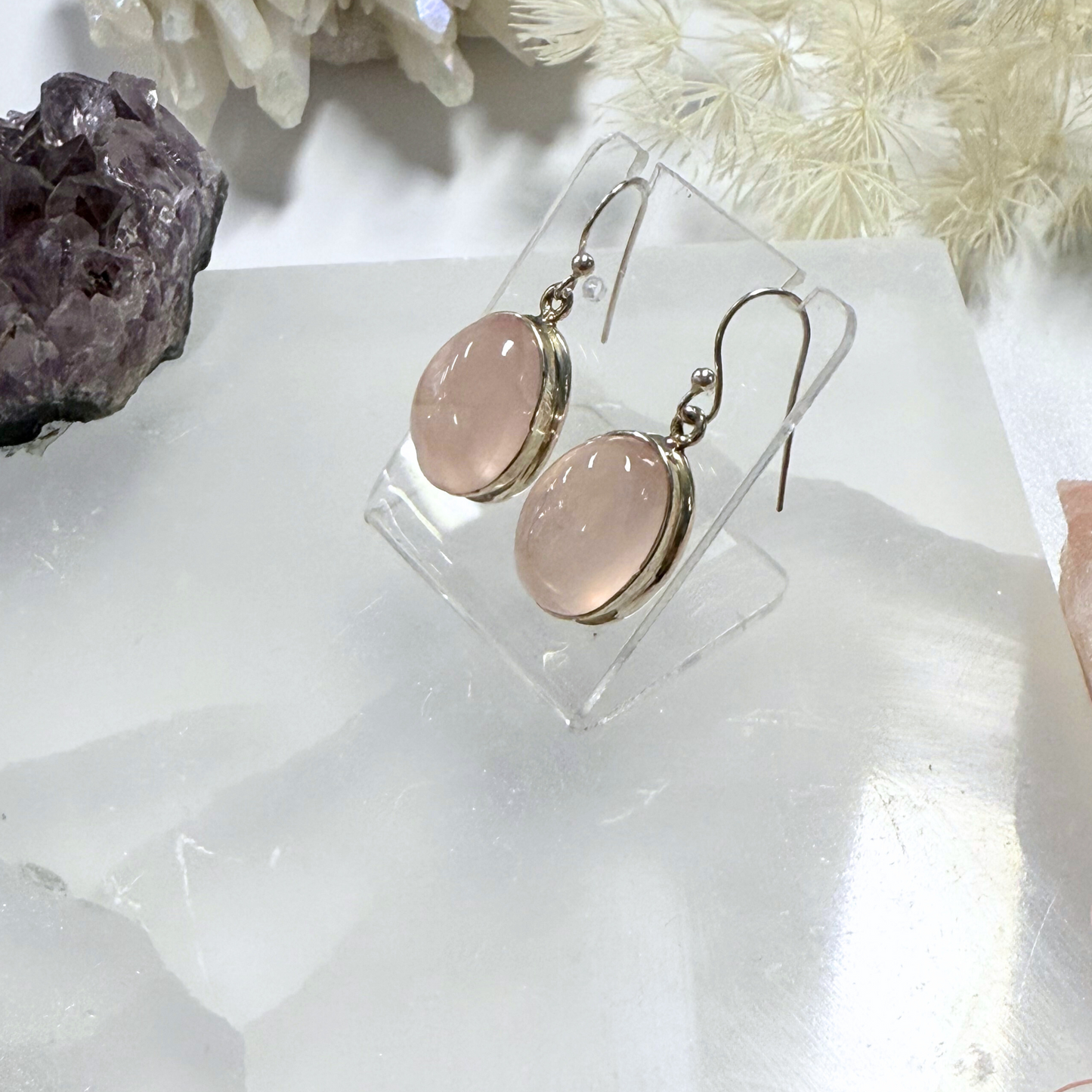 Rose gold earrings on a clear stand with a shell and crystals in the background