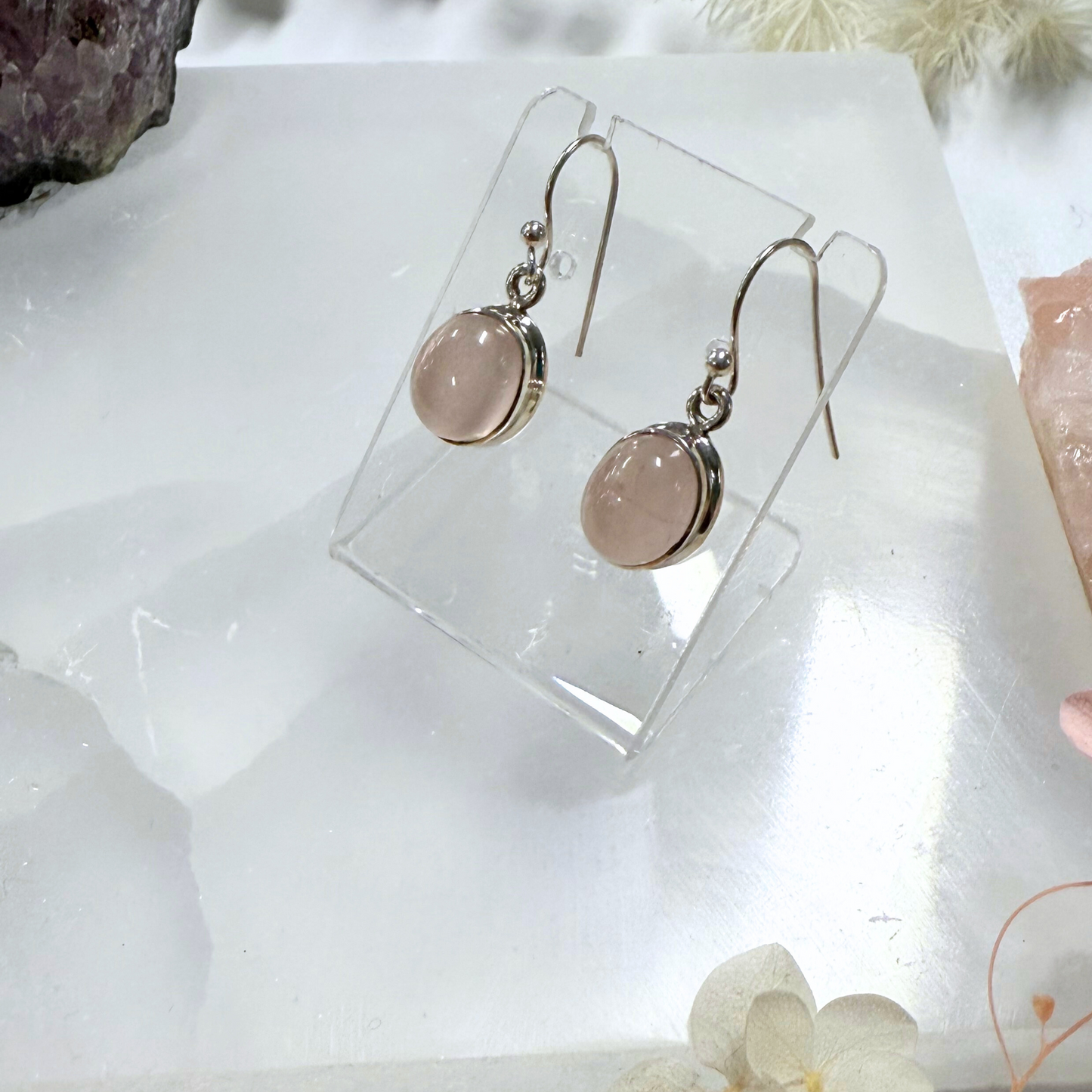 Pair of earrings with pink stones on a clear stand against a soft, blurred background.
