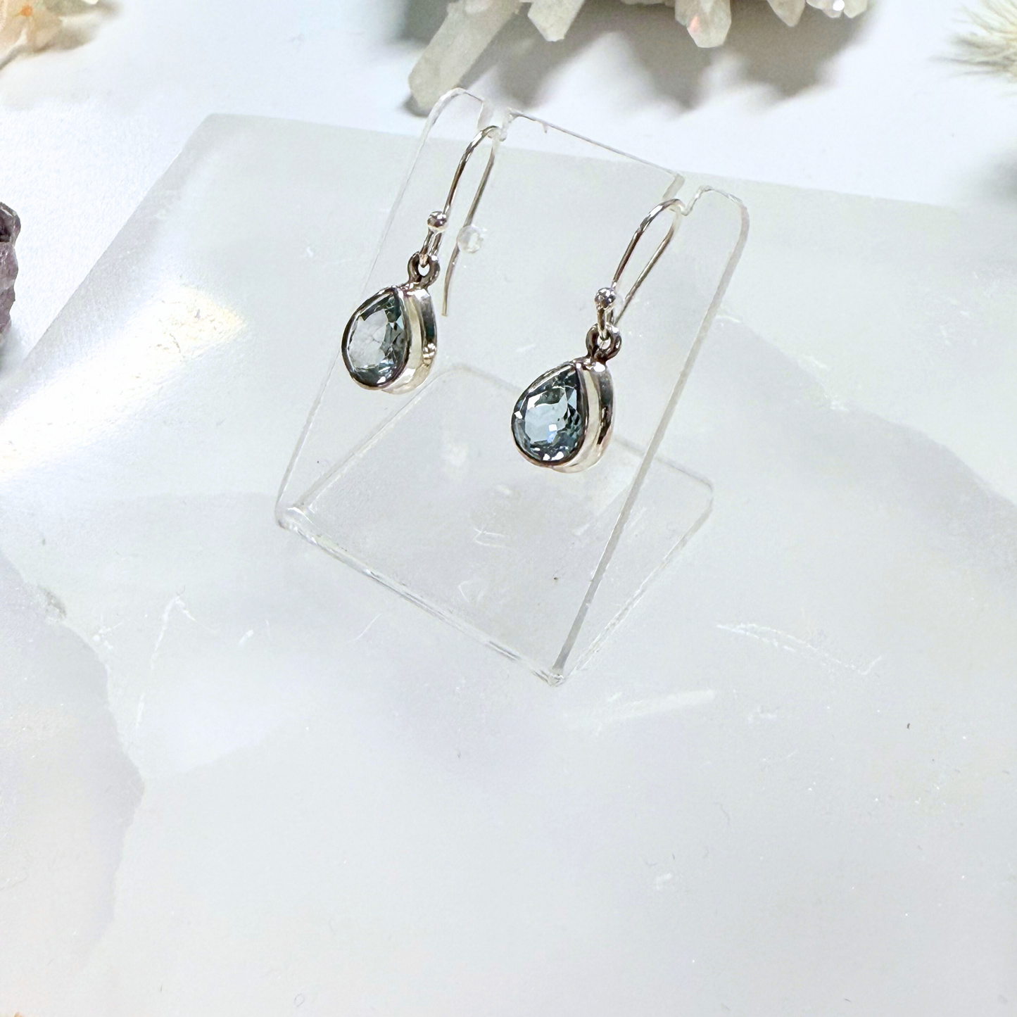 Teardrop-shaped earrings with gemstones on a clear stand against a white background