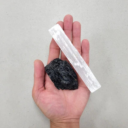 Hand holding a black stone and a white ruler against a gray background
